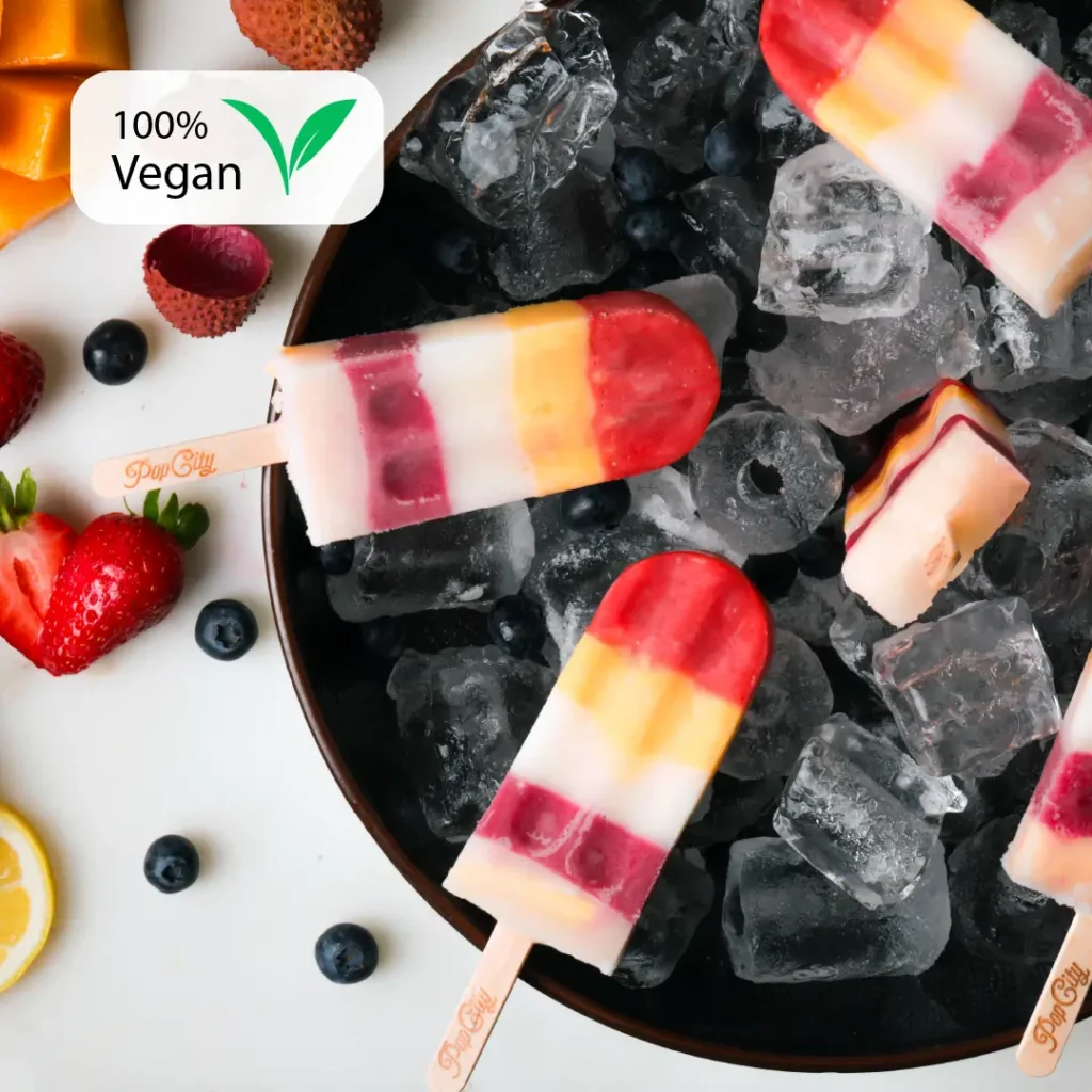 A bowl filled with ice cubes and colorful Fivesicle popsicles, each with five distinct layers of different flavors, surrounded by fruits like strawberries, blueberries, and lychees.