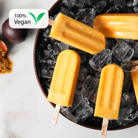 Bright orange passion fruit popsicles on a bed of ice, surrounded by halved and whole passion fruits, with a "100% Vegan" label in the top left corner.
