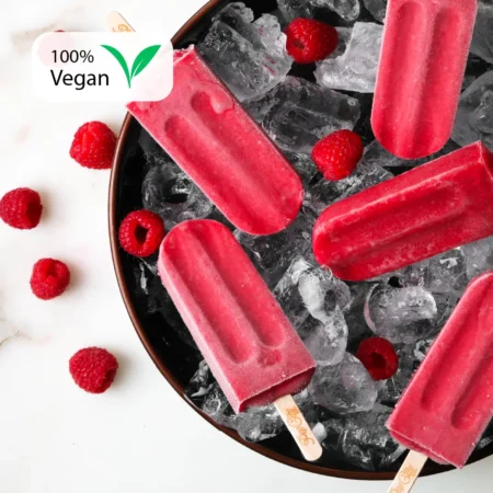 Raspberry-flavored popsicles on a bed of ice in a black bowl, surrounded by fresh raspberries, with a "100% Vegan" label in the top left corner.