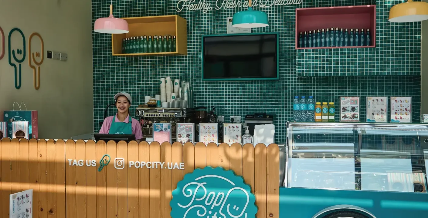 Interior of a colorful and inviting Popcity shop, featuring a wooden counter with a turquoise panel, a bicycle wheel, and the shop's name in English and Arabic.