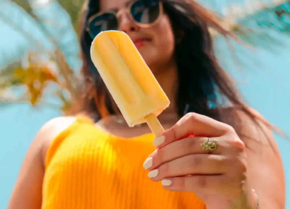 Person holding a yellow popsicle with a palm tree in the background