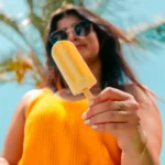 Person holding a yellow popsicle with a palm tree in the background