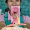 Hand holding a colorful fruit popsicle with kiwi and berries, branded Pop City stick, against a tiled wall