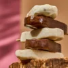 Stacked chocolate and vanilla popsicles on a wooden surface with a soft pink-beige background