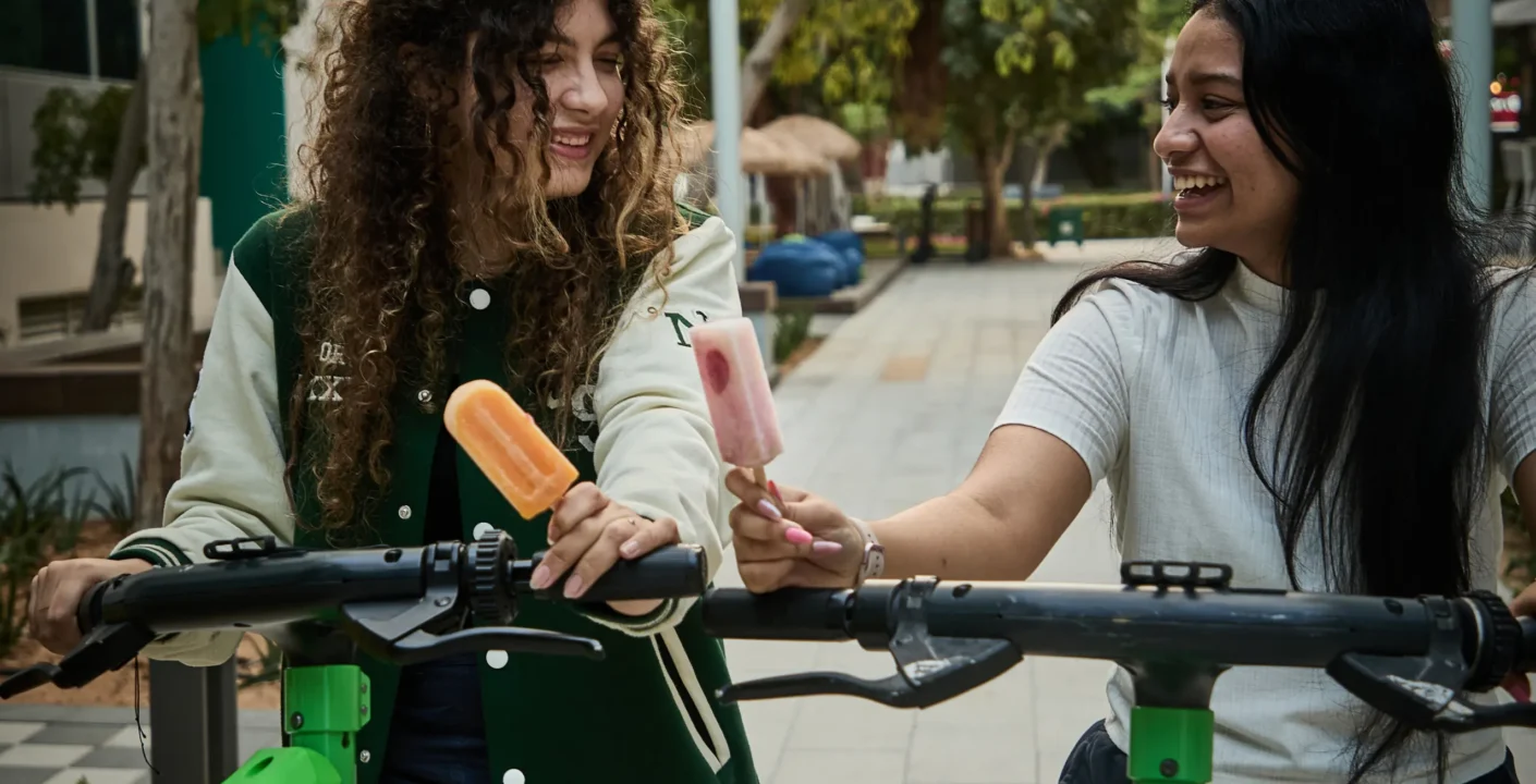 Two people enjoying popsicles while riding scooters outdoors in Dubai summer