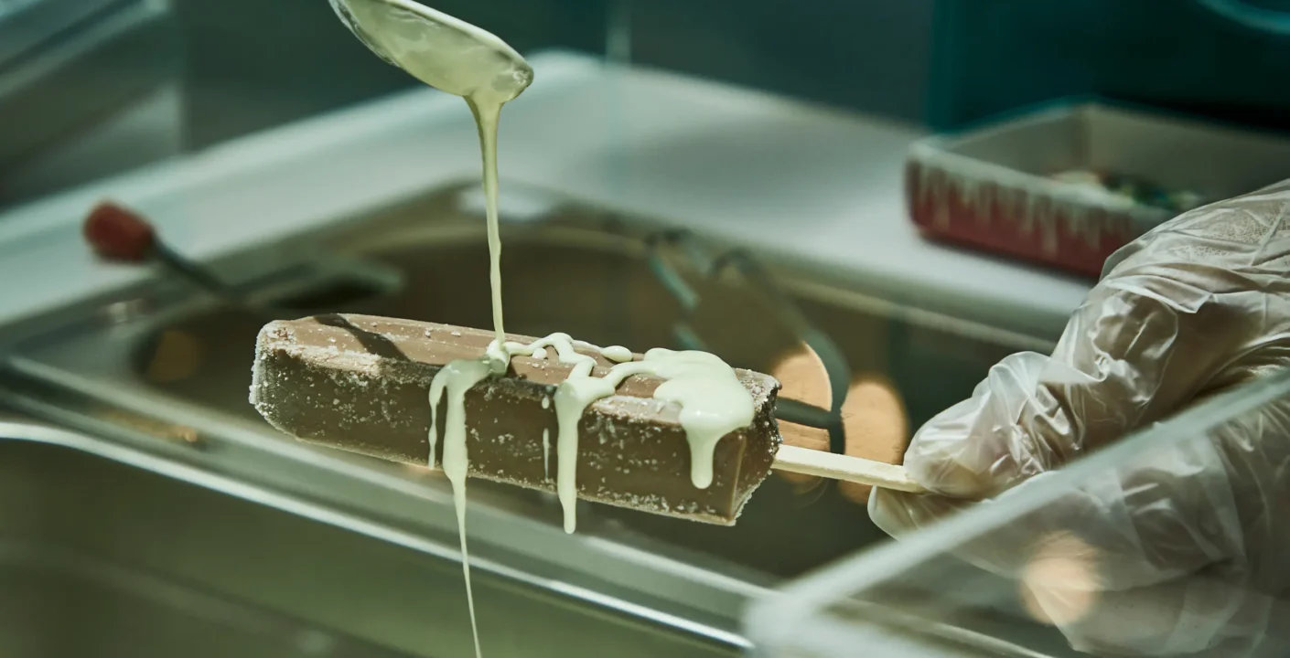 Hand drizzling white chocolate over a Pop City chocolate ice pop, a perfect dessert pairing for Dubai cafés.